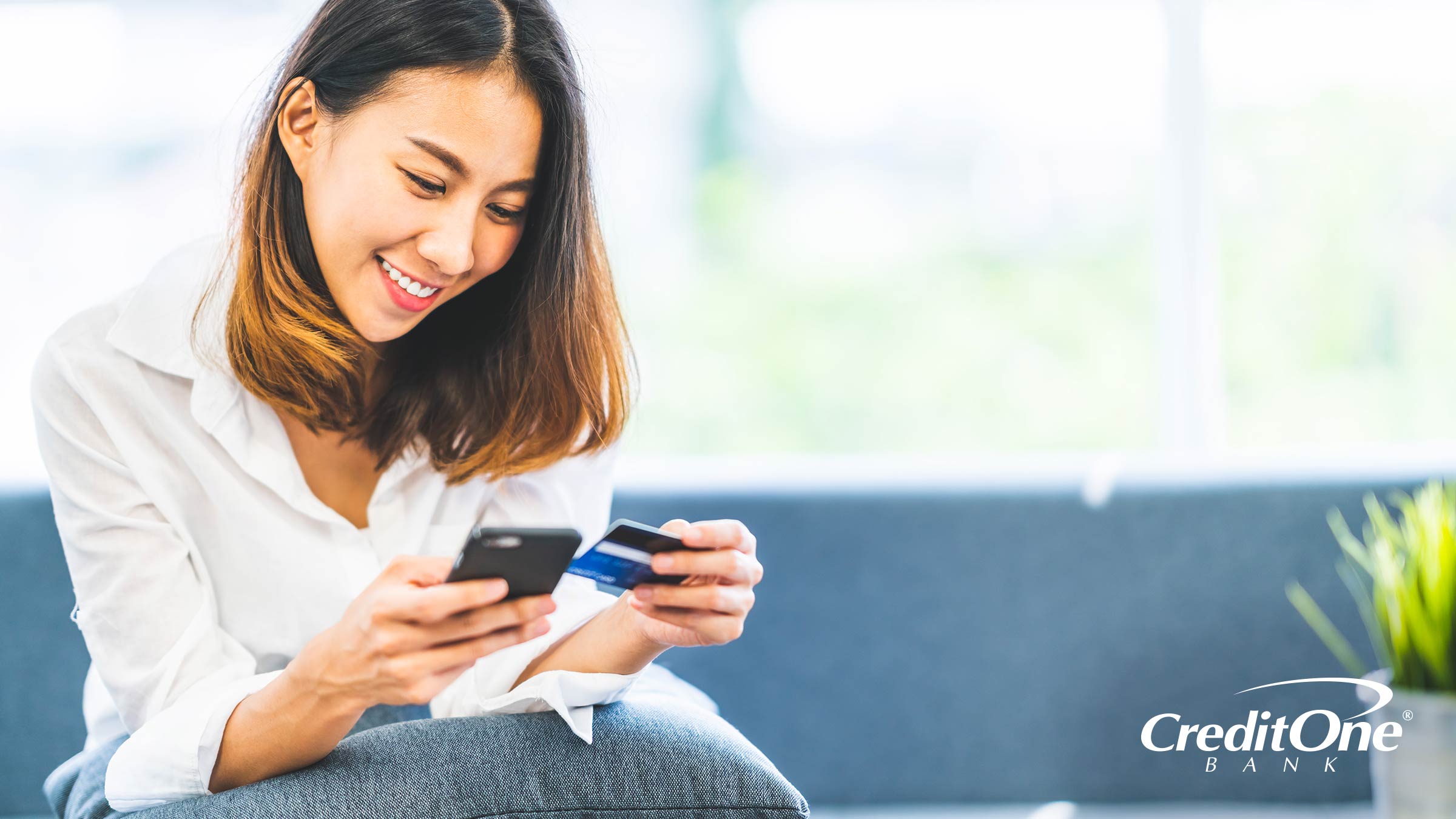 A woman holds her credit card while using her account mobile app, wondering how credit card payments work.